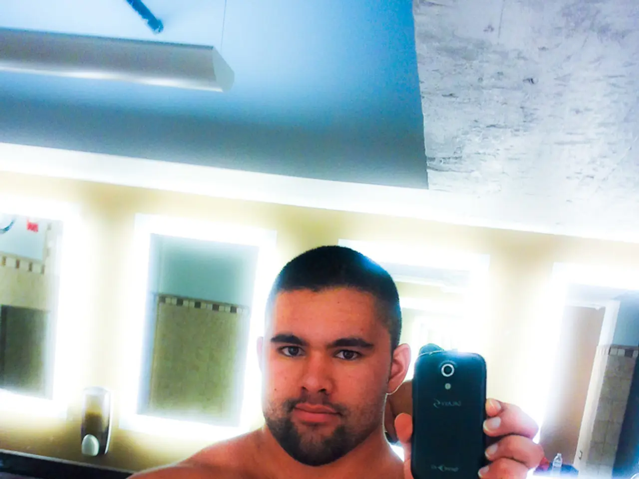 In this image the man is holding a camera phone in his hands. In the background of the image there...