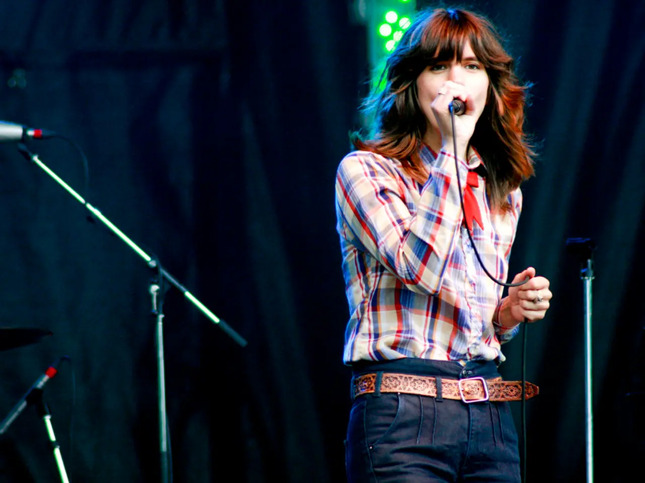 There is a woman holding a microphone on stage beside her so many other microphones.