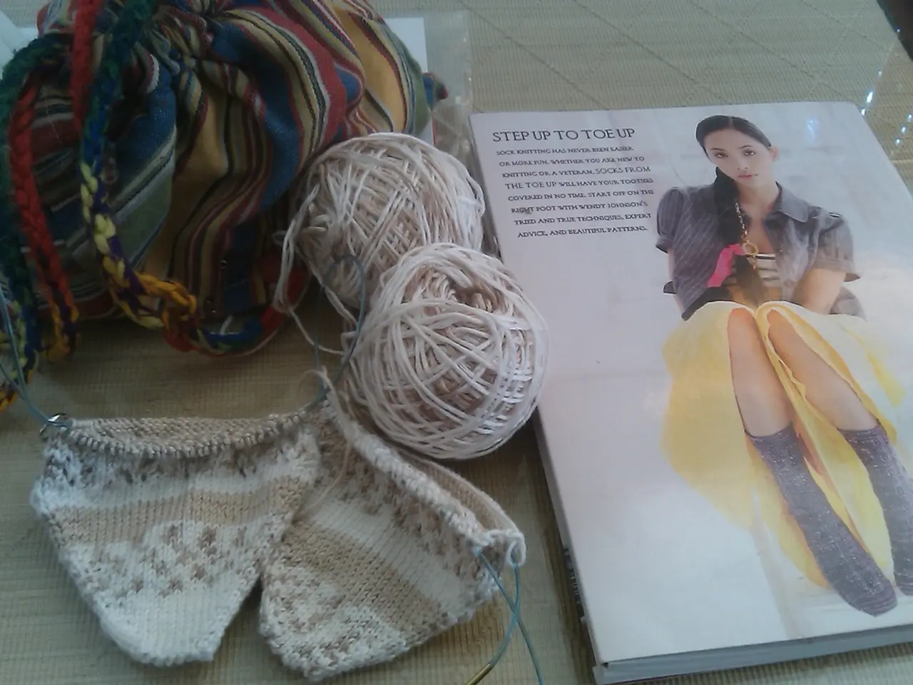 In this image there is a book, wool roll, cloth, papers on the table.