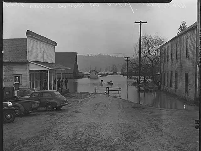 In the picture I can see some buildings, in between there is a pot beside some vehicles are being...