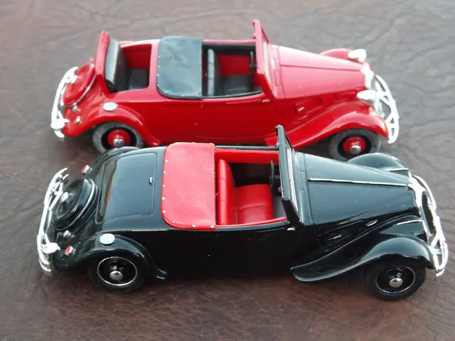 In this picture we can see two black and red color classic miniature car placed on the table.